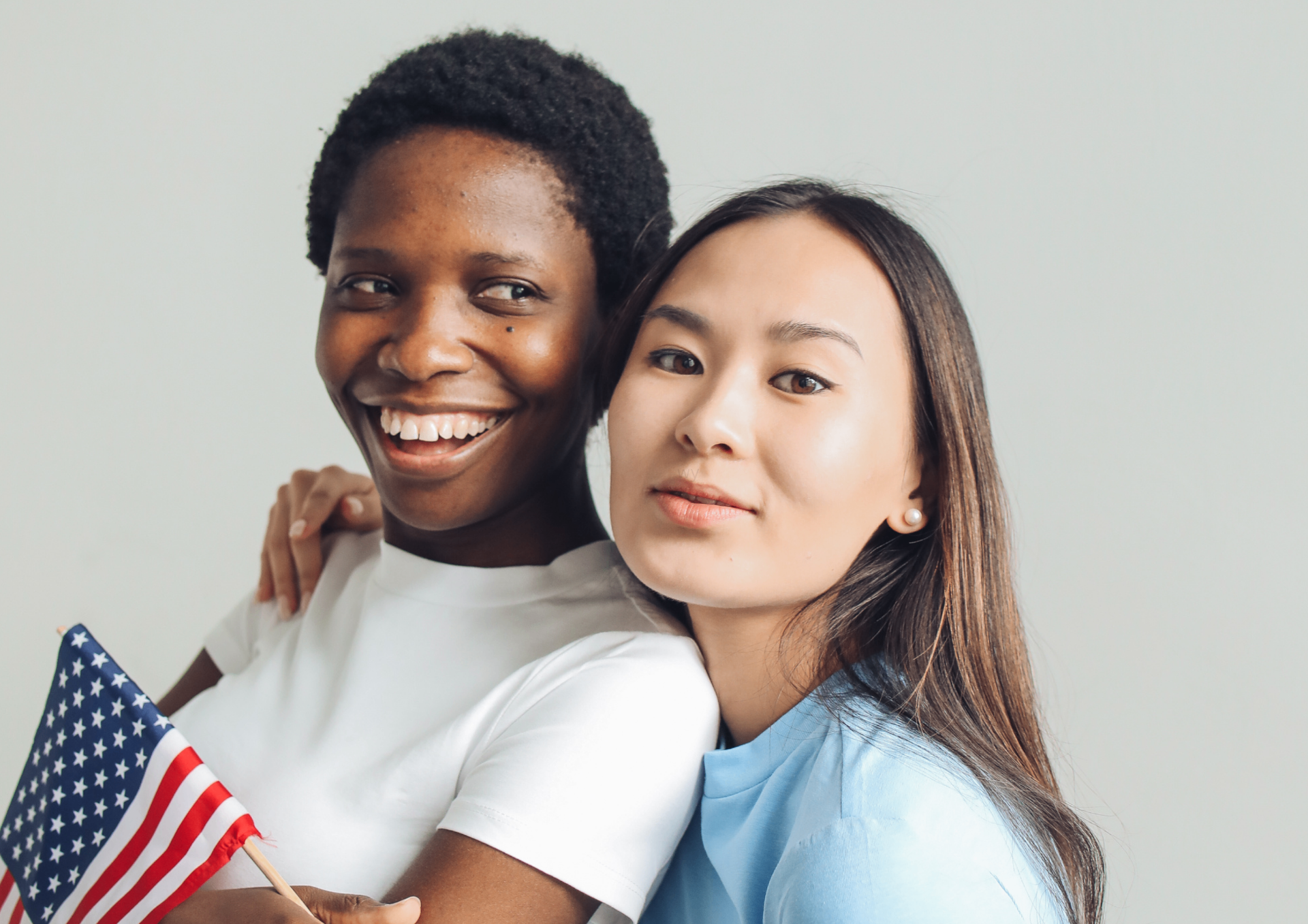Two smiling women, one holding a small American flag